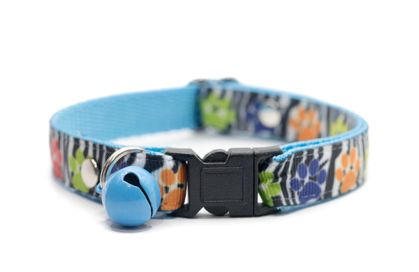 Cat collar with colorful paw print pattern and blue bell on a white background