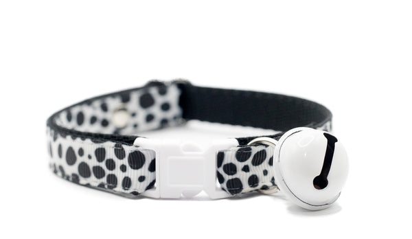 Cat collar with black and white paw pattern and bell on a white background