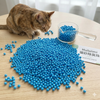 Cat interacting with blue cat litter beads on a table, with a scoop and packaging labeled