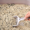 Hand using a white scoop to turn over cat litter in a tray