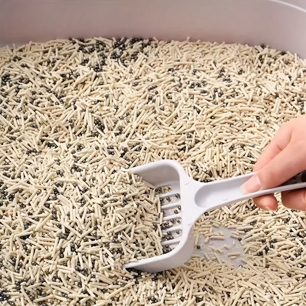 Hand using a white scoop to turn over cat litter in a tray